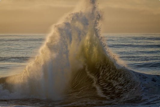 Powerful wave crashing on a beach with a golden sunset sky.